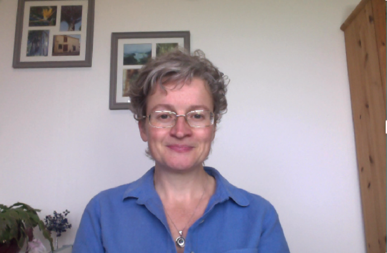 Rachael wearing a blue shirt sat in her office with a smile on her face.